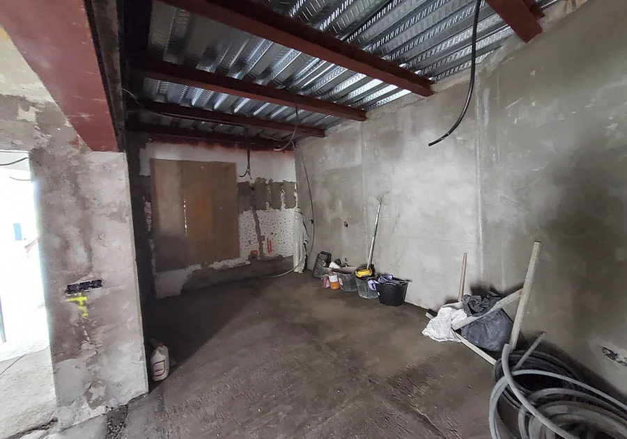 Estancia en proceso de reforma con paredes enfoscadas, techo de chapa colaborante y vigas metálicas visibles. Materiales y herramientas en el suelo. Foto propiedad de Vigasa.