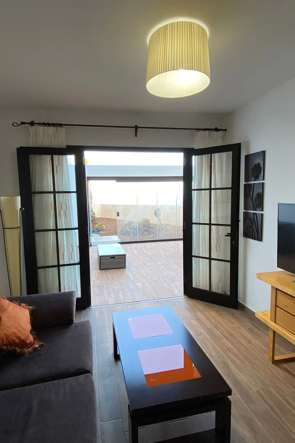 Salón reformado con suelo imitación madera, puertas acristaladas abiertas hacia terraza exterior con cerramiento de cristal. Proyecto realizado en Tenerife. Foto propiedad de Vigasa.