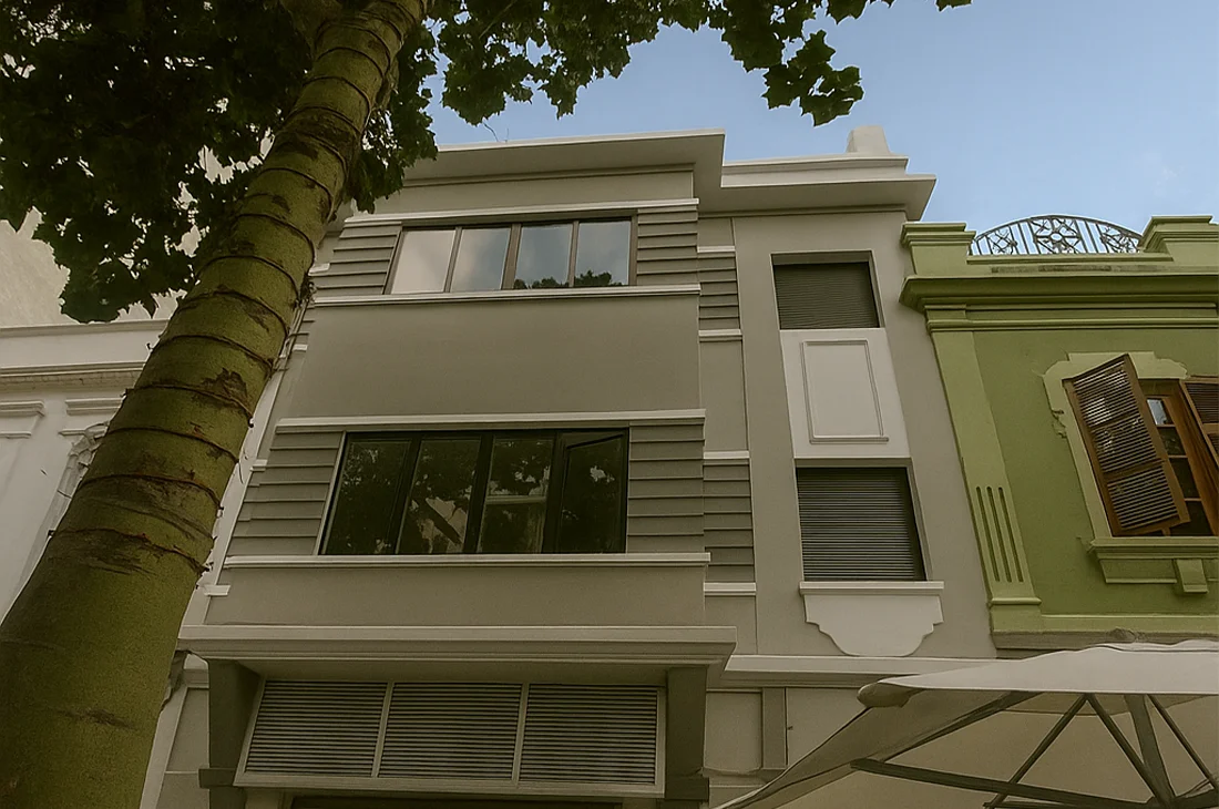 Fachada frontal de un edificio renovado de tres plantas, con acabado moderno en tonos beige y gris. Se destacan líneas horizontales, ventanas de aluminio y detalles arquitectónicos en relieve, integrados en un diseño limpio y simétrico. Proyecto ejecutado por Vigasa, especialista en construcción y servicio, con soluciones integrales para rehabilitación de inmuebles en entornos urbanos.