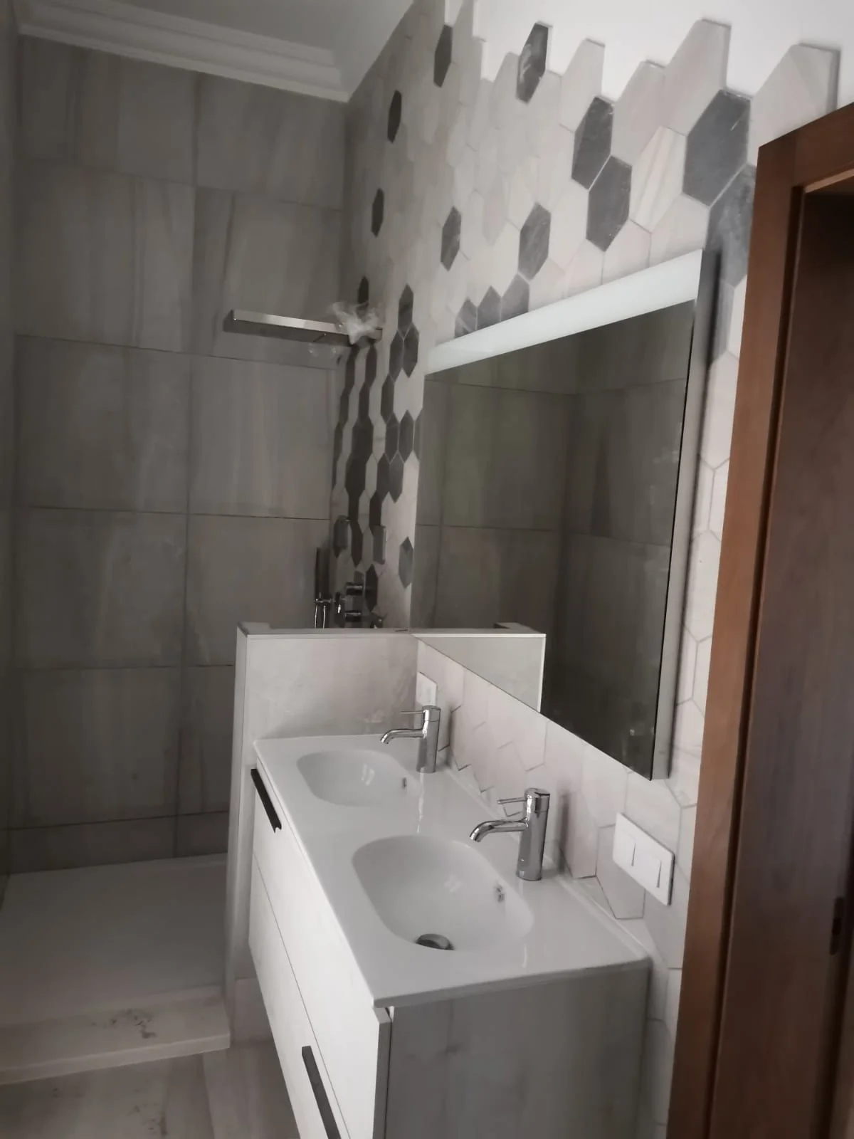 Baño reformado en Las Palmas con revestimiento cerámico, lavabo doble moderno y grifería cromada. Pared decorativa con azulejos hexagonales. Foto propiedad de Vigasa.